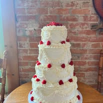 Four-tier white wedding cake with piped scrollwork and red roses