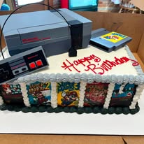 Birthday sheet cake decorated with retro video game cartridges and a console topper