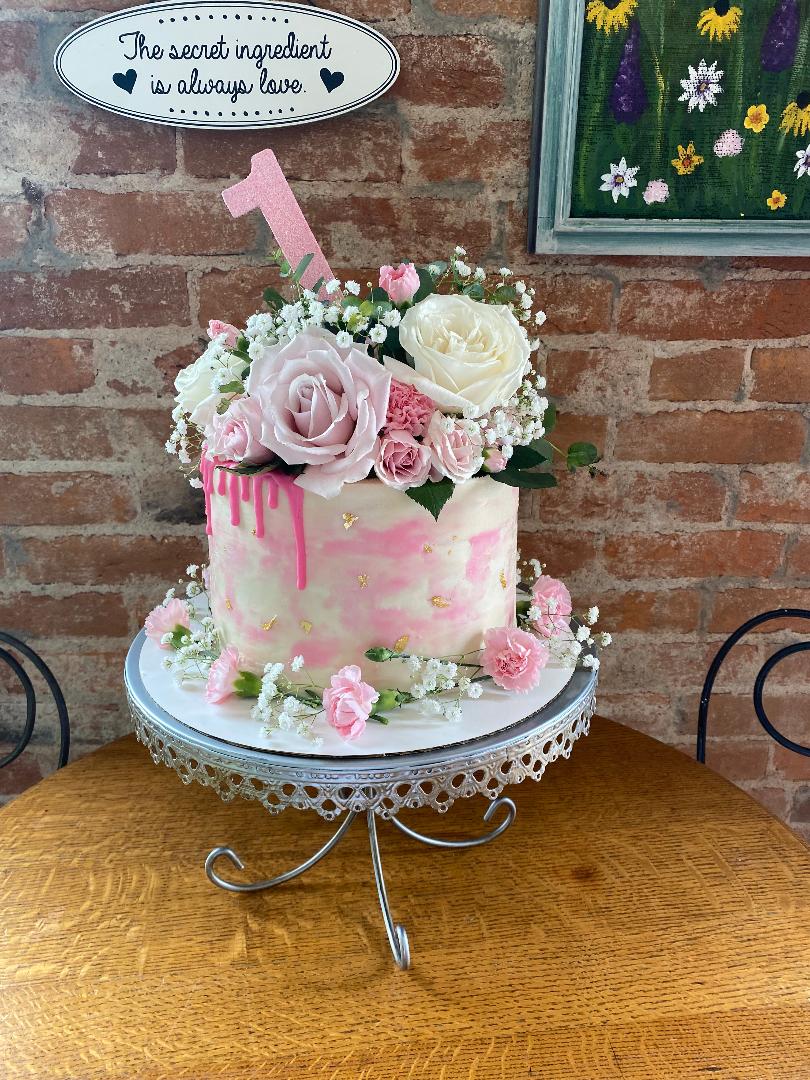 Pink and cream watercolor first birthday cake topped with fresh roses and baby's breath