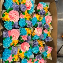 Tray of cupcakes piped with pink, purple, blue and yellow buttercream flowers